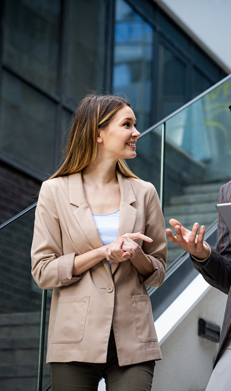 Eine Frau und ein Mann mit Tablet, beide im Business Look, stehen auf einer Treppe in einem modernen Unternehmen und unterhalten sich